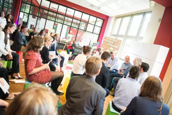 Meet and Change Infoveranstaltung, Teilnehmende sitzen auf bunten Hockern im Sitzkreis vor Pinnwand