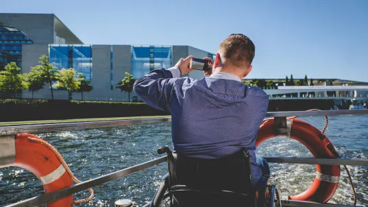 Auf dem Foto ist ein Mensch im Rollstuhl auf einer Schifffahrt zu sehen. 