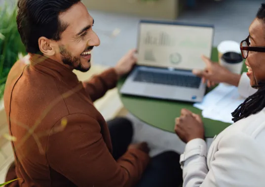 Zwei Personen im Gespräch, eine zeigt auf Diagramme auf einem Laptopbildschirm