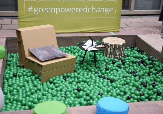 A sustainable stand with a green ball pit and seating made from reusable (cardboard, wood) resources.