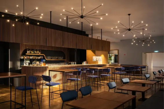 Moderne Bar mit Holztheke, blauen Stühlen und dekorativen Deckenleuchten.