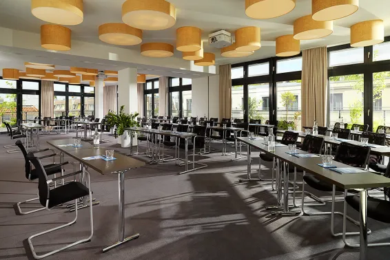 Heller Konferenzraum mit vielen Tischen, Stühlen und großen Fenstern