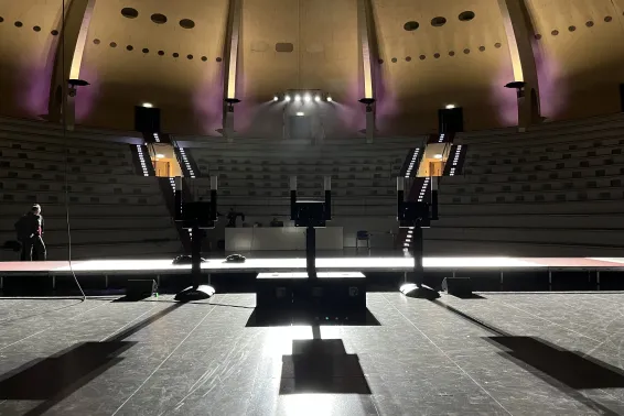 Leerer Vortragssaal mit Podium und lila Beleuchtung, Blick von der Bühne.