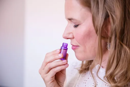 Frau hält lila Fläschchen unter die Nase und riecht daran, Augen geschlossen.