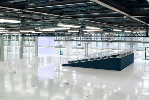 Große, leere Halle mit glänzendem weißen Boden und industrieller Decke.