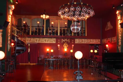 Roter Saal mit Kronleuchter, Bar, Bühne und Galerie, warm beleuchtet