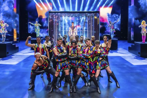 Tanzgruppe in bunten Kostümen auf einer hell erleuchteten Theaterbühne.