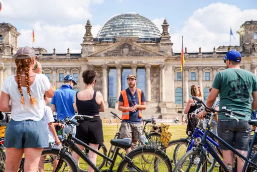 Gruppe von Radfahrern vor dem Reichstagsgebäude in Berlin bei sonnigem Wetter.