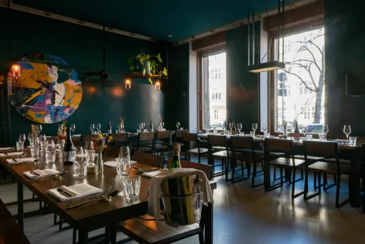 Modernes Restaurant mit gedeckten Tischen, großen Fenstern und dunkler Wandfarbe.