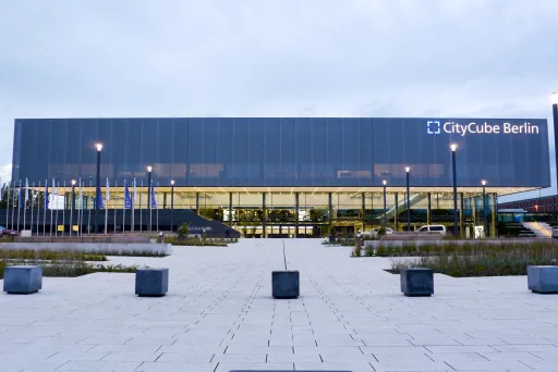Moderne Glasfassade des CityCube Berlin bei Dämmerung, beleuchtet und umgeben von Parkplatz.
