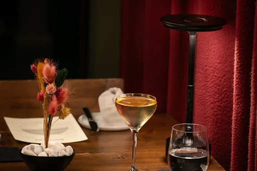 Elegant gedeckter Tisch mit Getränken, Speisekarte, Besteck und rotem Vorhang im Hintergrund.