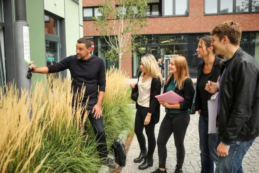 Eine Gruppe junger Leute hört im Freien einem Mann aufmerksam zu.