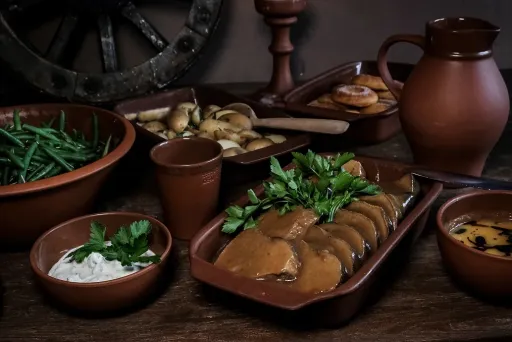 Rustikales Essen in braunen Keramiktellern, Bohnen, Brot, Bratensoße und Kräuter.
