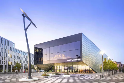 Modernes, kantiges Gebäude mit Glasfassade und großem Solarmodul auf dem Vorplatz