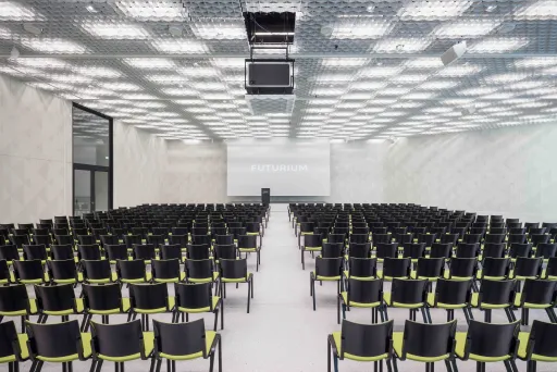 Leerer moderner Vortragssaal mit vielen schwarzen Stühlen und einer großen Leinwand vorne.