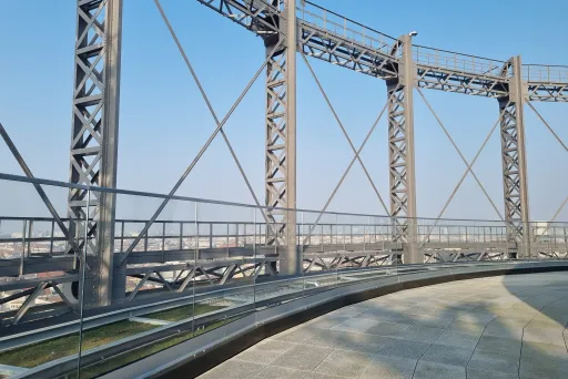 Stahlkonstruktion mit Glasgeländer, darunter Stadt im Hintergrund, blauer Himmel.