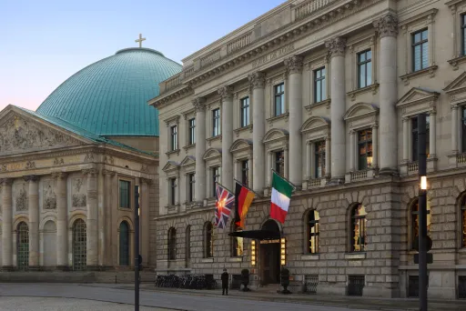 Historisches Gebäude mit vier Nationalflaggen, daneben eine Kuppelkirche im Hintergrund.