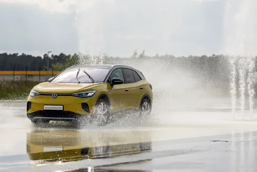 Gelbes Auto fährt durch große Wasserpfütze auf nasser Straße, Wasser spritzt hoch.