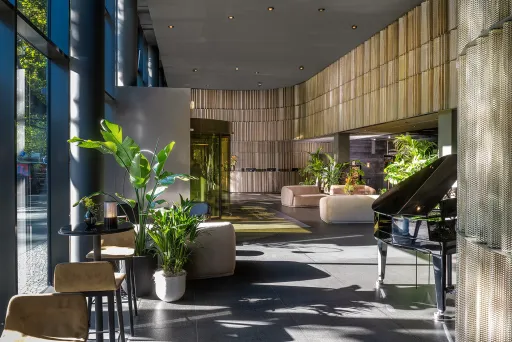 Heller Hotellobby mit großen Fenstern, Pflanzen, Sofas und einem schwarzen Flügel