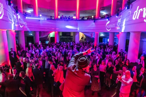 Menschenmenge auf einer Party mit bunter Beleuchtung und Musiker auf der Bühne.