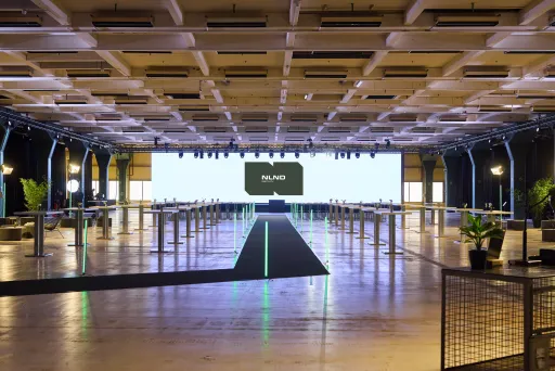 Großer, moderner Konferenzsaal mit Bühne, Lichtern und Begrüßungsbildschirm.