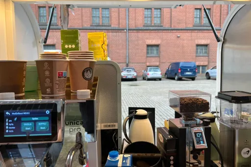 Kaffeemaschine und Pappbecher in einem mobilen Café, Blick nach draußen auf parkende Autos.