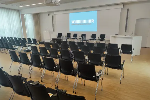 Leerer Konferenzraum mit schwarzen Stühlen und Bühne mit Leinwand.