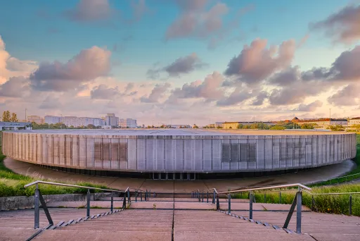 Rundes, modernes Gebäude bei Sonnenuntergang, vorne Treppen und Handlauf.