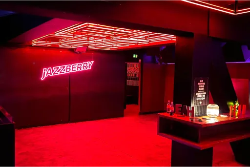 Bar mit neonroter Beleuchtung, moderner Einrichtung und leuchtendem Schriftzug an der Wand.