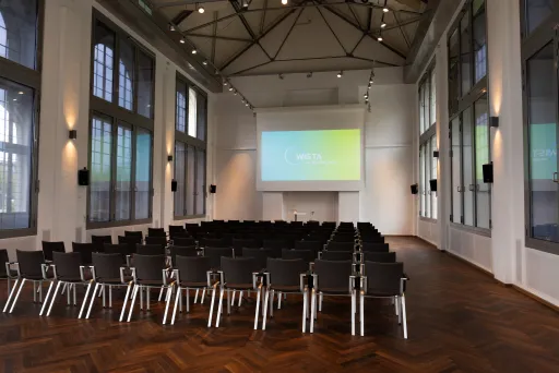 Leerer Konferenzraum mit Stuhlreihen und großer Leinwand vorne.