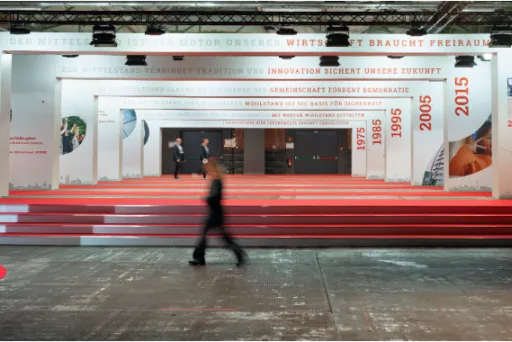 Person geht durch eine modern gestaltete Ausstellungshalle mit roten Stufen und weißen Wänden.