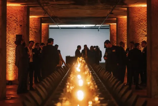 Stimmungsvoll beleuchteter Saal mit gedecktem Tisch und Menschen im Hintergrund.