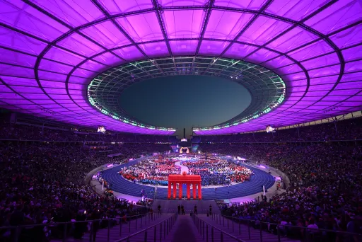 Das Berliner Olympiastadion mit violett beleuchtetem Dach, viele Menschen bei einer Großveranstaltung.