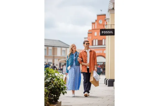 Paar spaziert lächelnd mit Einkaufstüten durch eine Einkaufsstraße bei bewölktem Himmel.