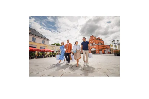 Vier Personen gehen lachend durch eine sonnige Fußgängerzone mit historischen Gebäuden.