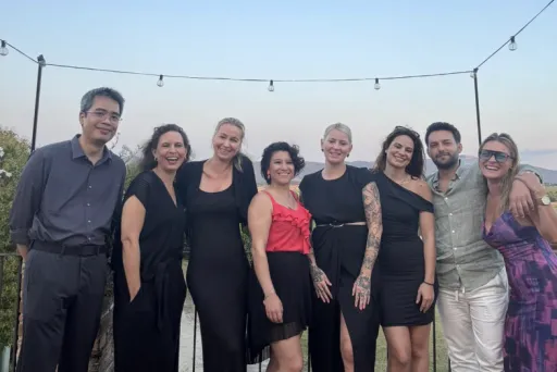 Acht Personen posieren lächelnd auf einer Terrasse bei Sonnenuntergang.