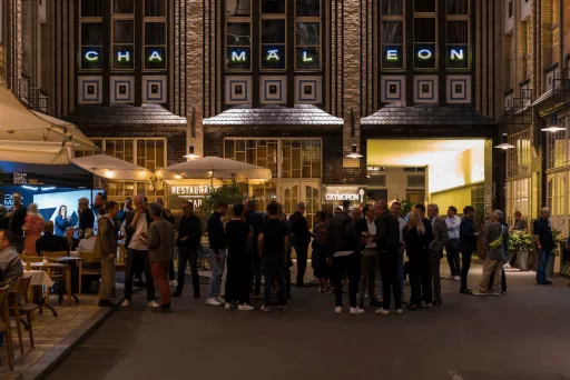 Menschenmenge vor einem beleuchteten Gebäude mit Schriftzug „Chamäleon“ am Abend.