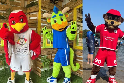 Drei bunte Maskottchen in Sportkleidung posieren fröhlich nebeneinander.