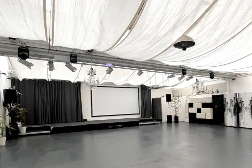 Helle leere Eventfläche in der Forum Factory Berlin mit Bühne, Vorhang und Projektionsleinwand.