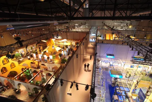 Große Messehalle mit bunten Messeständen und wenigen Menschen auf den Gängen.