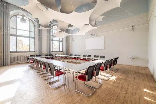 Heller Konferenzraum mit U-förmigen Tischen und modernen Stühlen.