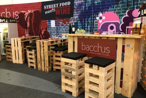 Bar aus Holzpaletten mit Hockern, bunte Wand mit Street-Art und Weinflaschen.