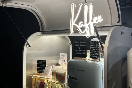 Leuchtendes Neon-Schild mit Herz, Getränke und Kaffeemaschine in einem mobilen Stand.