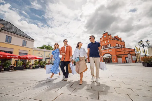 Vier Personen gehen lachend mit Einkaufstaschen durch ein sonniges Einkaufsviertel.