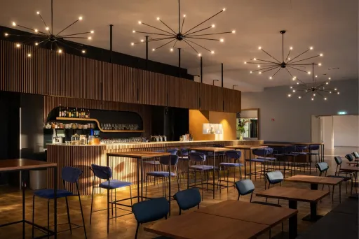 Moderne Bar mit Holztheke, blauen Stühlen und dekorativen Deckenleuchten.