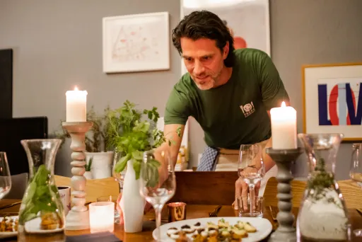 Mann deckt festlich gedeckten Tisch mit Kerzen und Speisen.