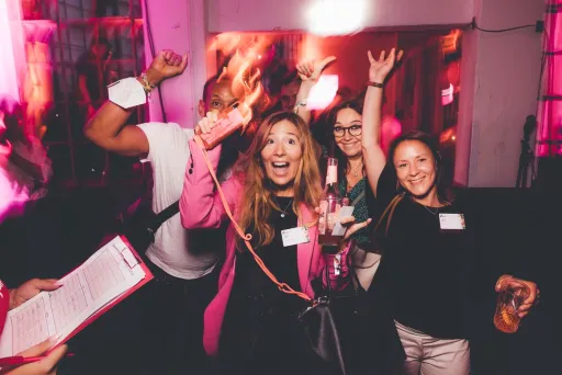 Vier fröhliche Menschen netzwerken in einem pink beleuchteten Raum.