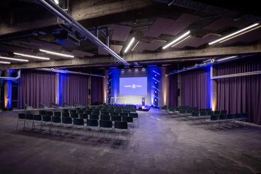 Leerer Konferenzsaal mit Bühnenbeleuchtung in Blau und Reihen von Stühlen.