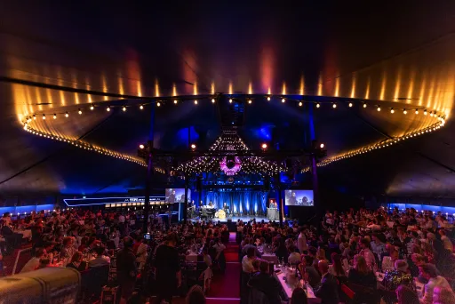 Der illuminierte, voll besuchte Saal im TIPI AM KANZLERAMT, Blick auf die Bühne davor Gäste an Tischen verteilt, nicht erkenntlich