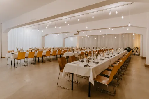 Festlich gedeckter Saal mit langen Tafeln, Holzstühlen und warmem Licht.